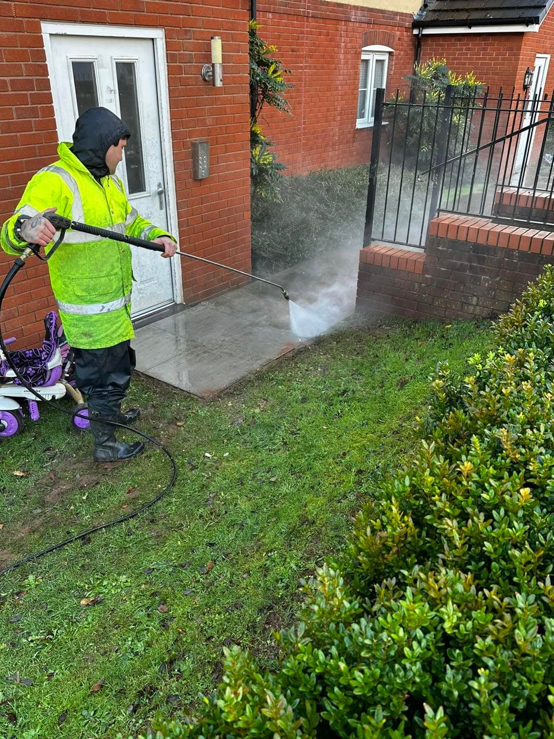 A crew member in a high-vis jacket jet-washing a concrete path